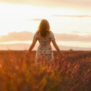 a woman with her arms out in a field whilst the sun is setting