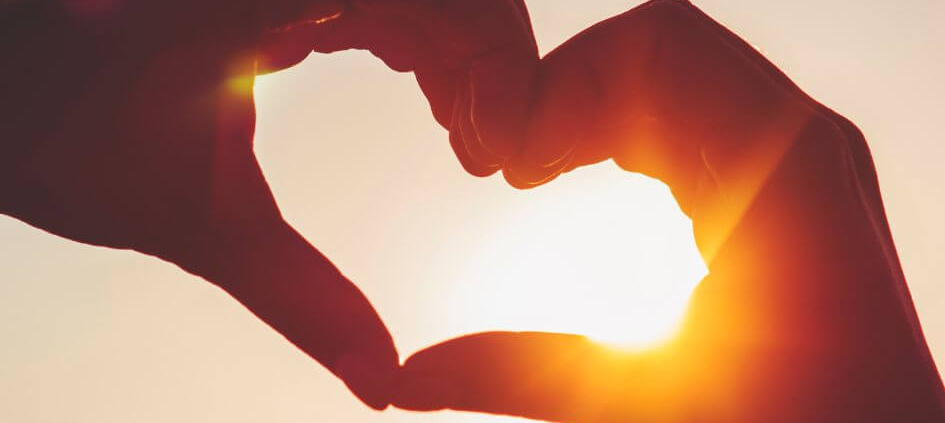 Two hands touching in the sunset, making a heart shape