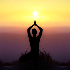 a silhouette of a woman in a yoga pose on a click edge with the sun setting in the distance